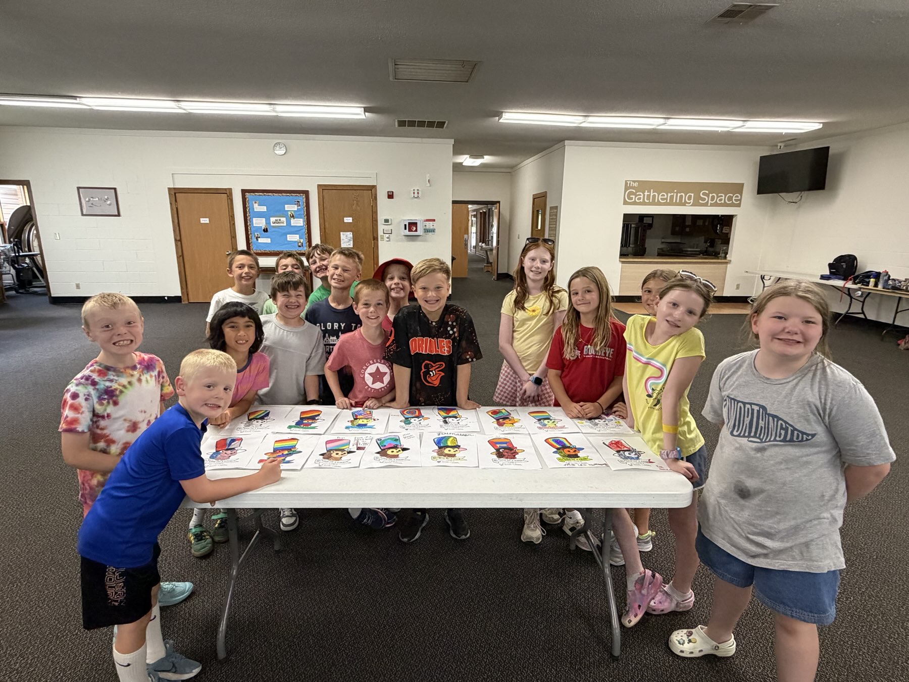 Sixteen campers gathered around a table of their finished colorful art projects
