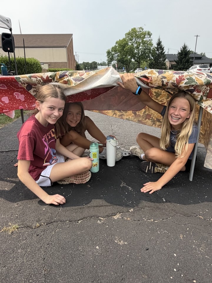 Three campers grinning from inside a tablecloth fort