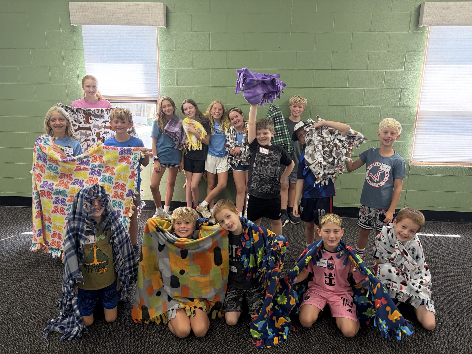 A big group of smiling campers holding up the fleece tie blankets they made