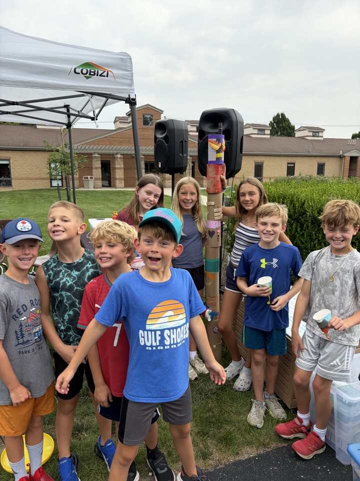A group of campers outside next to the decorated cardboard totem pole they made