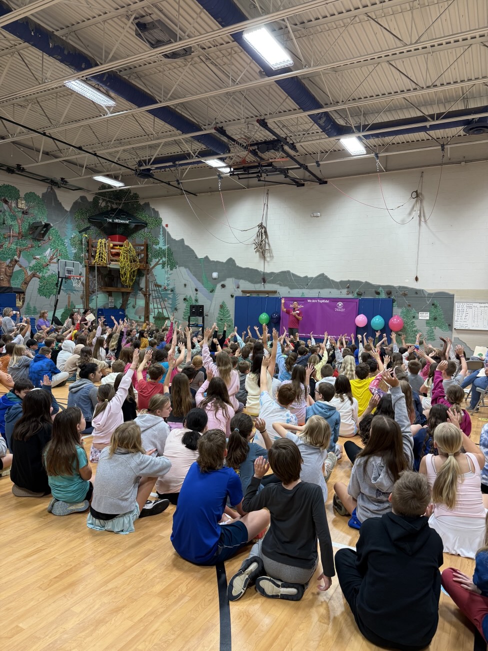 A gym full of students raising their hands during a TopKid assembly