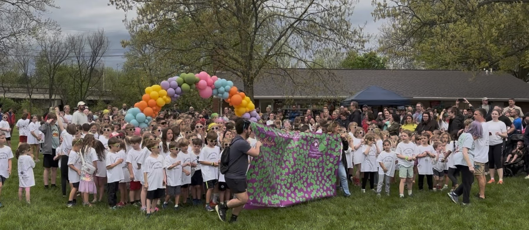 Students and families gathered outdoors under a balloon arch at a TopKid fundraising event