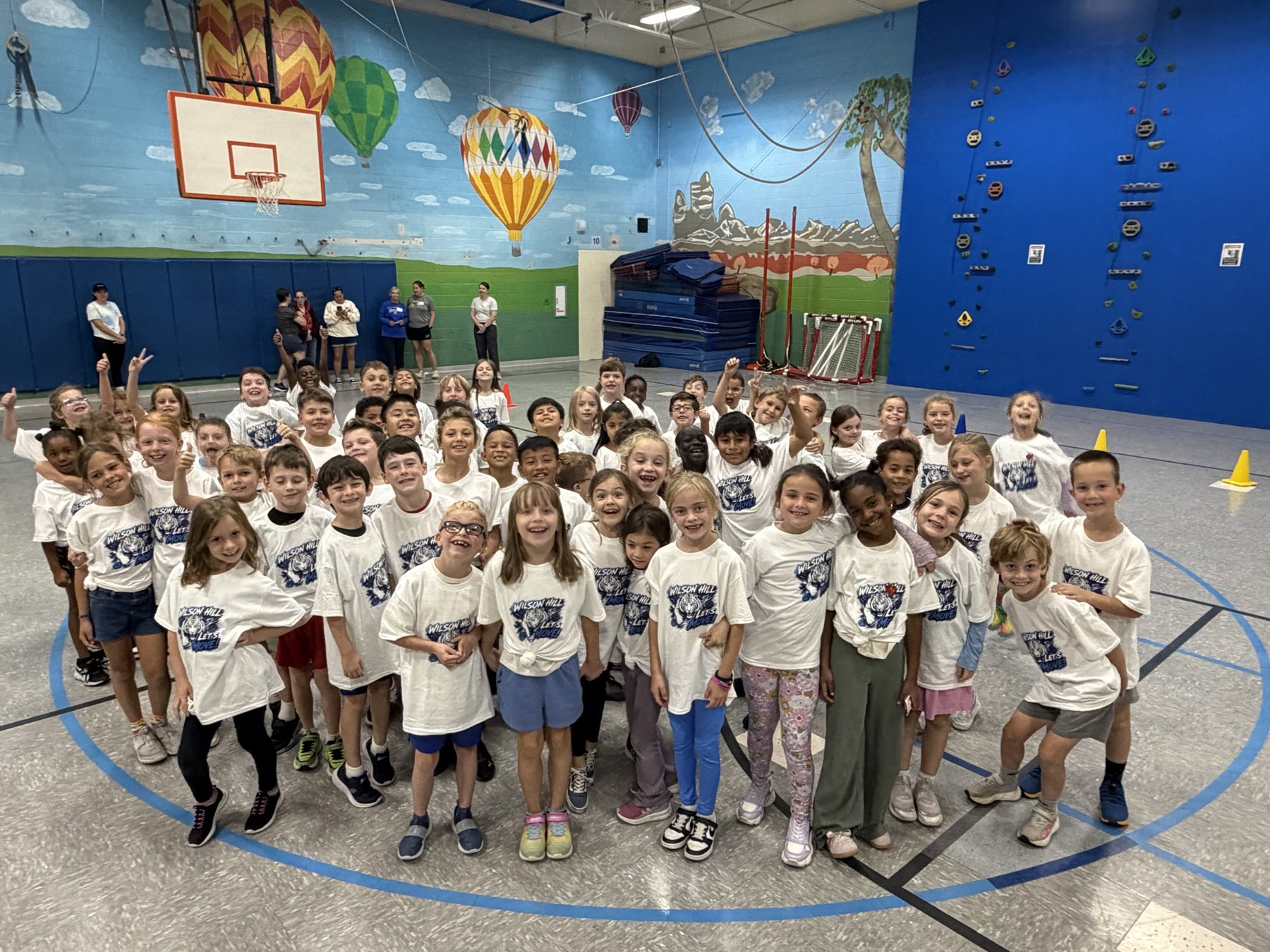 A big group of smiling students in matching event shirts in a school gym